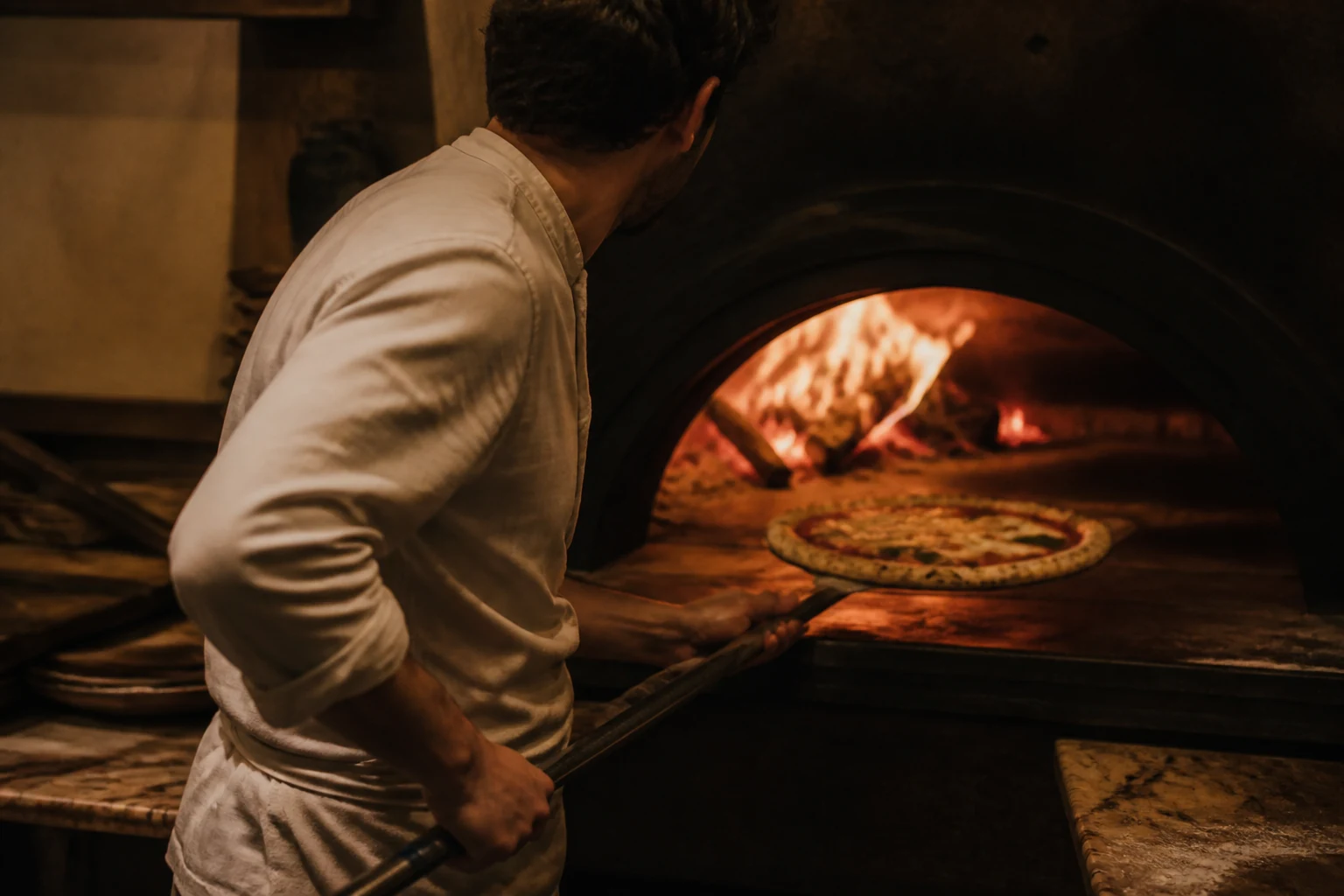 Le pizzaïolo devant les flammes du four à bois