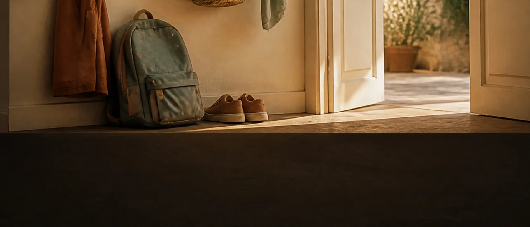 Entrée d’un logement en fin d’après-midi, cartable posé contre le mur